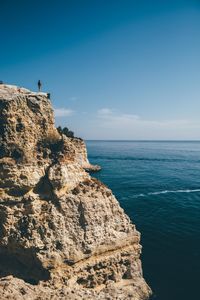 Rear view of man standing on cliff by sea against sky