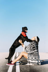 Woman with dog and skateboard against clear blue sky