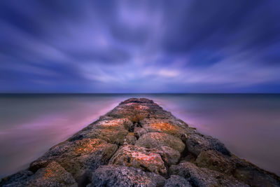 Rock on sea against sky at sunset