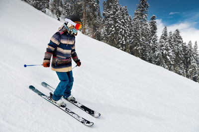 A skier in a striped jacket goes down the slope of the ski resort. active winter recreation, skiing
