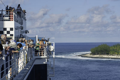 People standing by boats in sea against sky