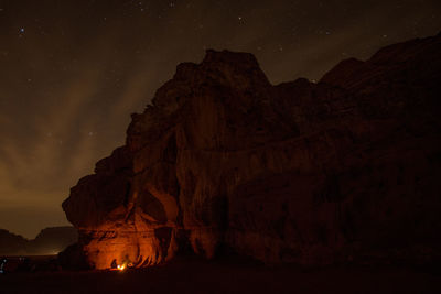 Fire by rock formations against sky at night