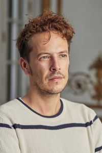 Handsome redhead male with wavy hair looking away in contemplation on blurred background