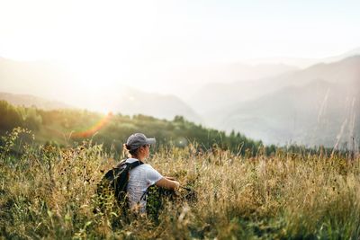 Rear view of woman sitting on field against mountain