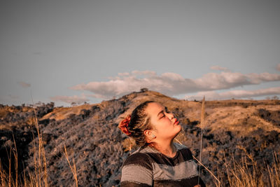 Young woman with eyes closed standing on mountain against sky