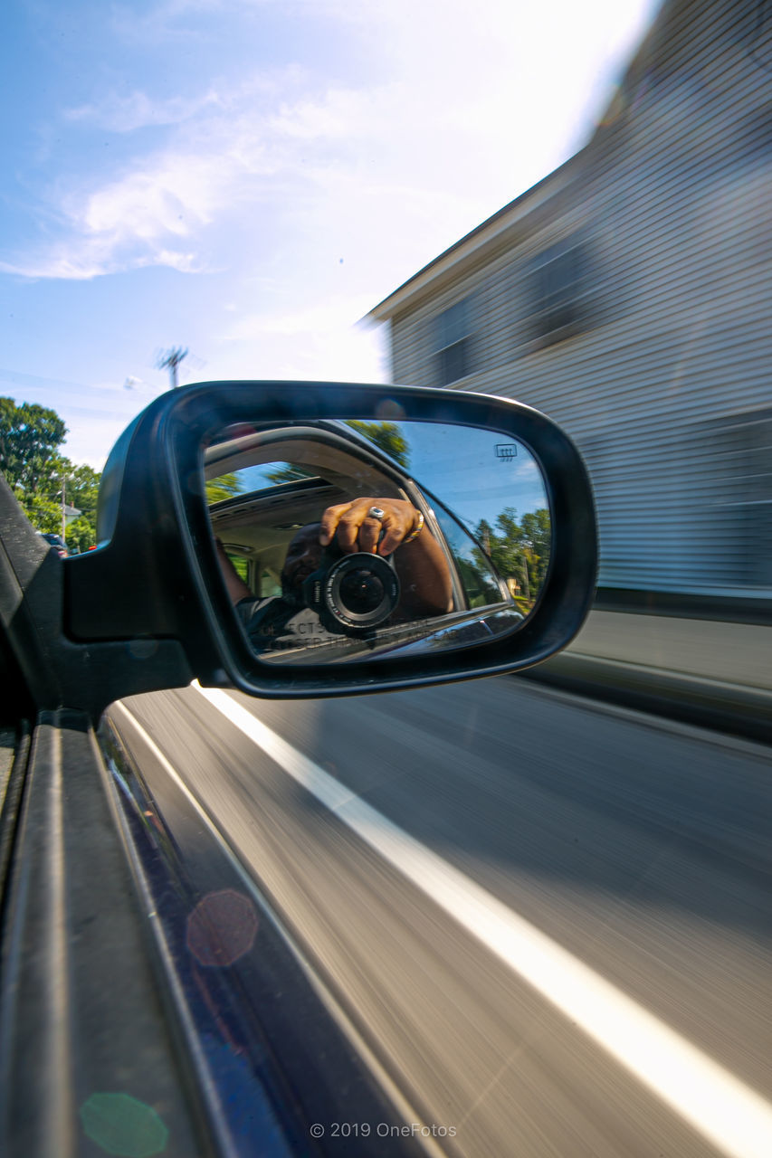 REFLECTION OF CAR ON SIDE-VIEW MIRROR AGAINST SKY SEEN THROUGH GLASS WINDOW