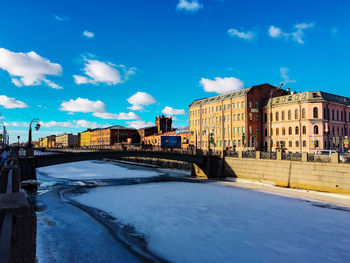 Snow covered road in city against blue sky