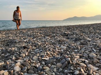 Full length of woman walking at beach against sky during sunset