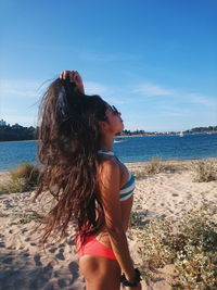 Side view of young woman standing at beach against sky