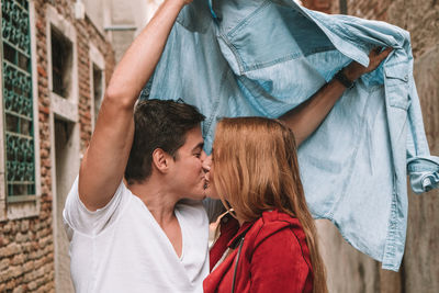 Young couple kissing under shirt by wall