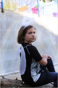 Side view of cute girl wearing halo and costume wing sitting outdoors