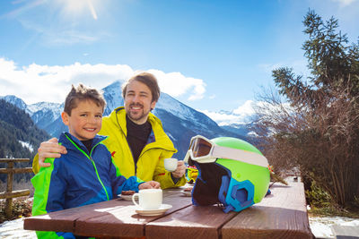 Portrait of smiling friends sitting on table against sky