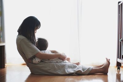 Side view of mother and baby sitting on floor at home