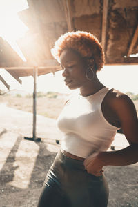 Confident african american female with dyed hair in trendy outfit standing near weathered structure on sunny summer day on street