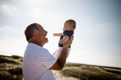 Grandfather holding grandson while standing on beach