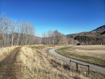 Road amidst field against clear blue sky