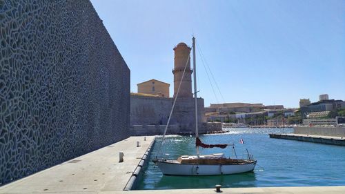 Sailboats in sea by buildings against clear sky