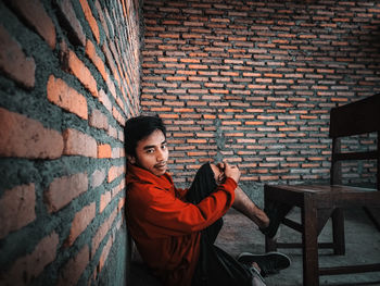 Portrait of young woman sitting against brick wall