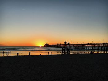 Silhouette pier on beach against clear sky during sunset