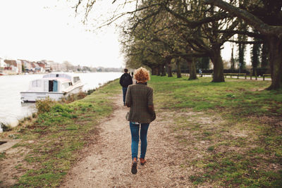 Rear view of man and woman walking at riverbank against sky