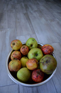 High angle view of blemished apples in fruit bowl on hardwood floor