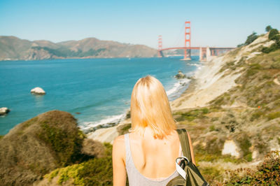 Rear view of woman with backpack looking at golden gate bridge against sky