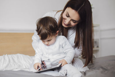 Happy mother using tablet computer with baby boy while sitting on bed