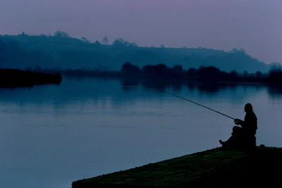 Silhouette man fishing in lake against sky