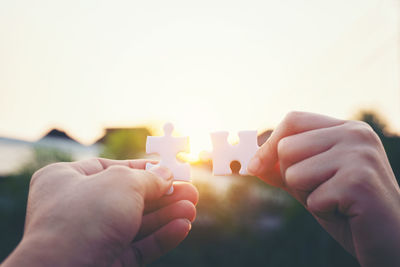 Cropped hands of people holding jigsaw pieces against sky during sunset