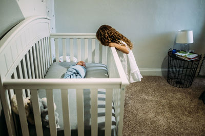 Young girl looking over the crib at newborn sibling