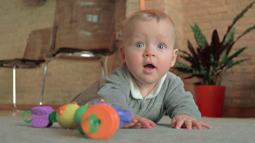 Portrait of cute baby boy with toy on floor