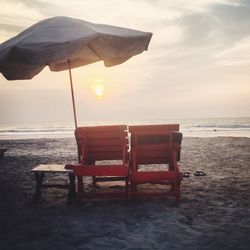 Chair on beach against sky during sunset