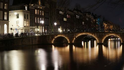 Illuminated arch bridge reflecting in canal at night