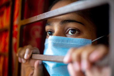 A bored asian young girl wearing a protective surgical face mask at looking through the window.