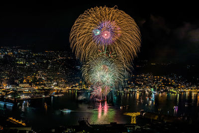 Firework display over illuminated city against sky at night