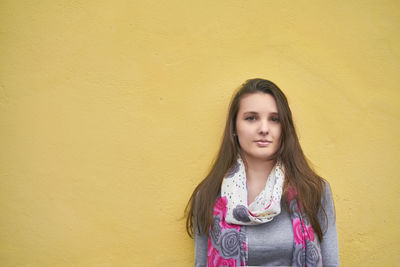 Portrait of young woman standing against yellow wall