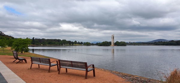 Empty bench by lake against sky