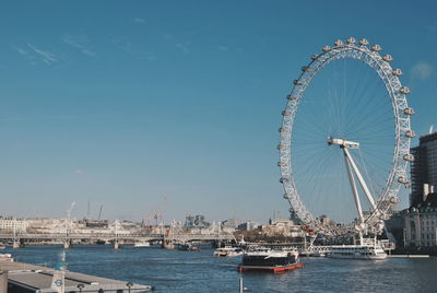 Ferris wheel by river in city against clear blue sky