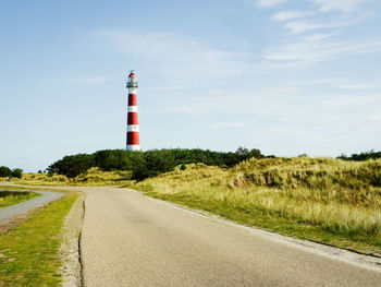 Road leading towards lighthouse amidst field against sky