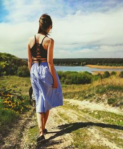 Rear view of woman walking on field against sky