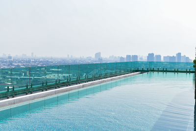 Swimming pool by city against sky