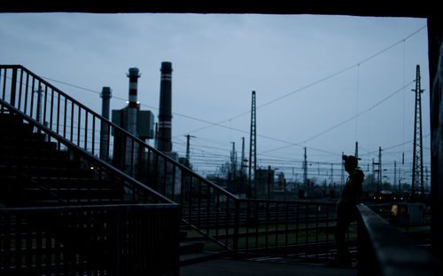 Man walking on railing in city against sky
