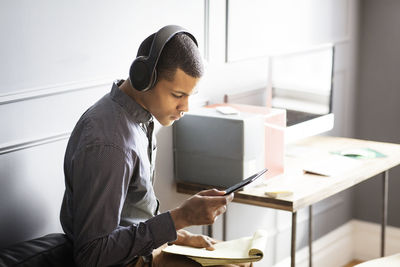 Side view of businessman listening music while using tablet computer in office