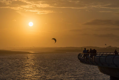 Rear view of person paragliding over sea against sky during sunset