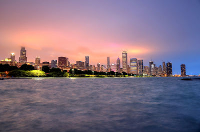 Sea by buildings against sky during sunset