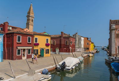 Boats in canal amidst buildings against clear sky