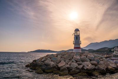 Lighthouse at sea shore against sky during sunset