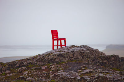Empty red chair on rock formation against clear sky
