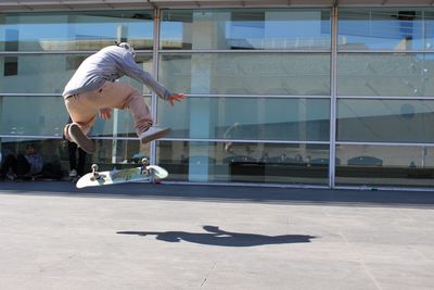 Man jumping while skateboarding on footpath in city