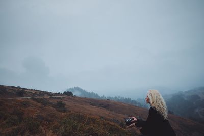 Woman with camera on landscape against sky